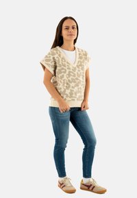 Maglione beige a collo a V con una sottile stampa animale, tessuto a maglia, maniche corte; abbinato a jeans skinny blu e sneakers beige.