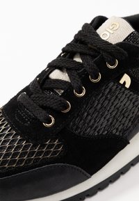 Czarne sneakersy wykonane z zamszu i siateczki, z złotymi oczkami i teksturowanym wzorem, na kontrastowej białej podeszwie.