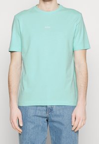 Ljusblå bomullströja med korta ärmar, rund halsringning och liten vit "BOSS"-logotyp på bröstet. Bärs med ljusa denimjeans.