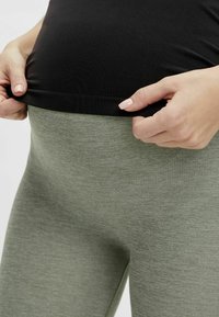 Grå leggings gjorda av mjukt, stretchigt tyg med hög midja. En svart topp är delvis synlig och håller i midjan.