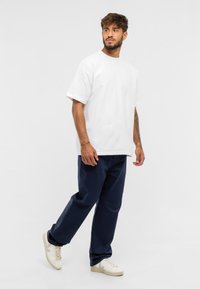 Biela kr短zv衩 t-shirt s krátkym rukávom v kombinácii s tmavomodrými nohavicami a béžovými teniskami. Má voľný strih a minimalistický dizajn bez vzorov.