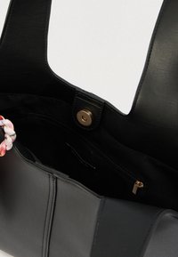 Μαύρη δερμάτινη τσάντα τύπου tote με δύο ανθεκτικές λαβές, στο εσωτερικό διαθέτει τσεπάκι με φερμουάρ και κλείσιμο με μπρούτζινο κούμπωμα. Ανάγλυφο με λουλούδι σε μία λαβή.