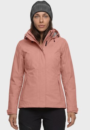 Frau trägt eine pinke Winterjacke mit Kapuze und eine schwarz-weiß gestreifte gestrickte Mütze und steht vor einem schlichten Hintergrund.
