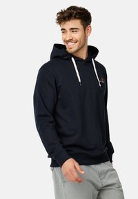 Mørkeblå hoodie med snor, prydet med et lille logo på brystet. Fremstillet af blødt materiale, har den en afslappet pasform og ribbede manchetter.
