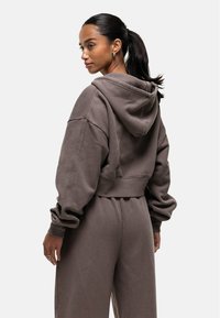 Bruine cropped hoodie met een capuchon, ruime mouwen en een losse pasvorm. Gladde textuur en een minimalistisch ontwerp zonder zichtbare logo's of patronen.