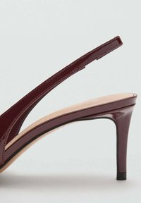 Pantofii cu toc din piele lucioasă burgundă, cu vârf deschis, curea subțire la glezna și toc înalt de tip stiletto; textură netedă și design minimalist.