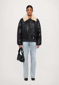 Veste bomber en cuir noir avec un col en fourrure crème, pull gris, jean droit bleu clair et un petit sac noir.