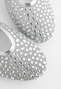 Sølv slip-on sko med en tekstureret overflade prydet med mange store cirkulære rhinestones, der giver en glitrende, reflekterende overflade.
