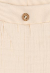 Hellbeige Stoff mit einem gerippten elastischen Bund. Verfügt über einen Holzknopf mit einem X-Muster in der Mitte zum Verschließen. Glatte Textur.