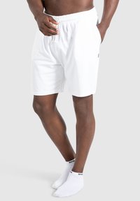 Weiße Baumwollshorts mit einem elastischen Bund und Kordelzug, ausgestattet mit Seitentaschen und einem dezenten Logoakzent. Tragen Sie dazu weiße Knöchelsocken.