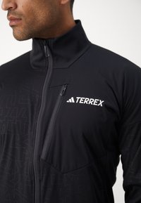 Zwarte tussenlaag jack met ritsluiting, hoge kraag, textuurpatroon en een linkerkant borstzak met logo.
