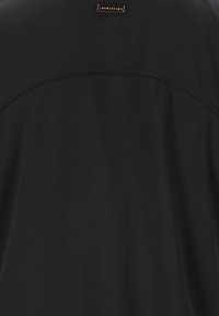 Schwarzes Sportshirt mit glatter Textur, dezentem Muster, genähten Details und einem kleinen metallischen Logo auf der Rückseite.