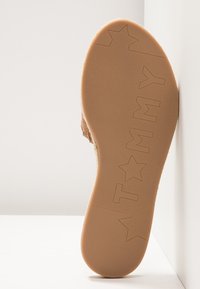 Semelle d'une chaussure couleur beige montrant des lettres embossées formant "Tommy" avec des formes d'étoiles sur un fond clair.