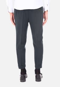 Pantaloni su misura verde scuro con una texture liscia, dotati di tasche laterali, orlo arrotolato e bottoni discreti in vita.