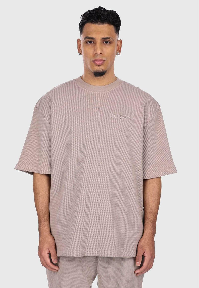 T-shirt court à manches courtes, en rose pâle, avec un col rond. Présente un logo brodé subtil sur la poitrine. Texture douce, coupe décontractée.