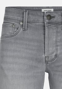 Jean en denim gris avec poches avant, passants de ceinture, fermeture à bouton et étiquette Jack & Jones visible à l'intérieur de la ceinture.