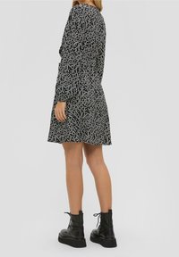 Černé šaty s bílým květinovým vzorem, dlouhými rukávy a rozšířeným spodním okrajem. V kombinaci s masivními černými šněrovacími kotníkovými botami. Hladká textura látky.