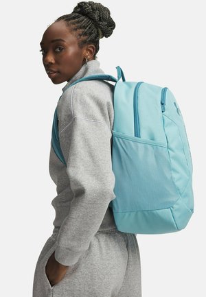 Turkooizen rugzak met een gestructureerd ontwerp, een meshvak en gevoerde bandjes, gedragen over een grijze sportoutfit, met de nadruk op de duurzaamheid ervan.
