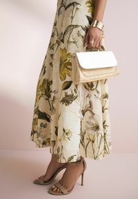 Abito maxi floreale nei toni crema e giallo; borsa intrecciata beige; sandali con tacco nudo; bracciale a fascia dorato; anelli come accenti.