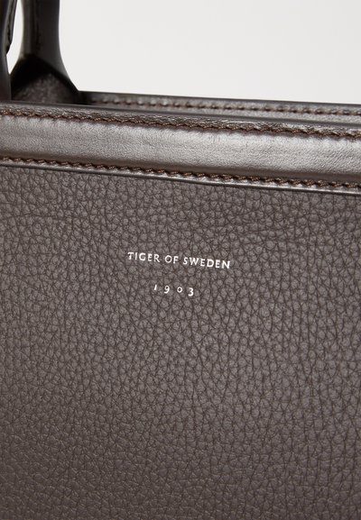Pruun nahkkeen kott, millel on tekstuuriga viimistlus, kontrastset õmblust ja valget embosseerimist "TIGER OF SWEDEN 1903".
