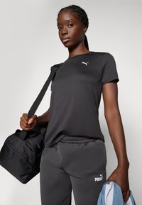 Svart treningst-skjorte med logo, kombinert med grå joggebukser og svart treningsbag. Glatt stoff, kortermet, avslappet passform.