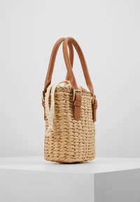 Borsa in paglia intrecciata con manici e dettagli in pelle marrone chiaro, forma cilindrica, nastro di chiusura beige regolabile, superficie testurizzata.