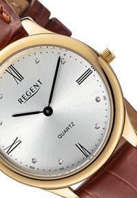 Montre en quartz en ton or avec un cadran argenté, des index d'heure noirs et des accents en faux diamant. Bracelet en cuir brun à la finition texturée.