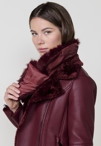 Bordo umjetni krzneni ovratnik s glatkom satenskom podlogom, u kombinaciji s kožnom jaknom s patentnim zatvaračem sprijeda i bočnim džepovima.