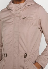 Jasno różowa kurtka z kapturem, z pełnym zapięciem z przodu, kieszenią na zamek błyskawiczny na piersi oraz regulowanymi sznurkami w talii. Gładka faktura, casualowy design.