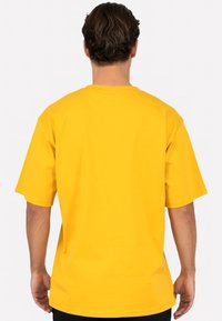 T-shirt jaune à manches courtes, col rond et texture lisse. Design simple sans motifs ni accents visibles.