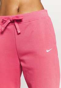 Rosa Sweatpants aus weichem Stoff verfügen über einen Kordelzugbund und ein kleines weißes Nike-Swoosh-Logo auf der linken Seite.
