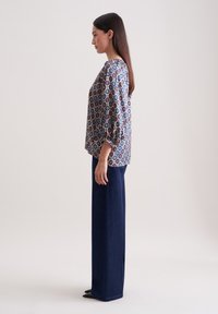 Knopf-bedeckte Bluse aus gemustertem Stoff in Blau- und Rottönen, kombiniert mit hoch-taillierten dunkelblauen Jeans, schlank geschnitten mit geradem Bein.