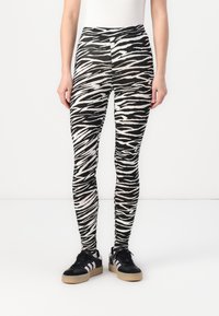 Zebraprint legging in zwart-wit, met een hoge tailleband en een strakke pasvorm, gecombineerd met zwarte sneakers met witte accenten.