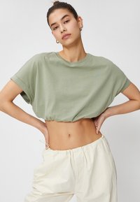 Afskåret grøn bomulds T-shirt med opfoldede ærmer, parret med let krämfarvede bukser med elastisk talje. Glat tekstur, afslappet pasform.