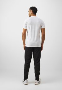White short-sleeve top with a fitted design, paired with loose-fitting black pants and white athletic shoes featuring black stripes.