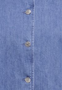 Modro denim blago z navpičnim nizom treh dekorativnih srebrnih gumbov z vtisnjenim cvetličnim vzorcem.