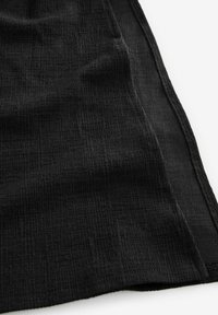 Tissu noir texturé drapé, présentant un motif de froissement subtil. Les bords montrent des coutures, avec une apparence douce mais structurée.