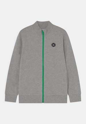 Chaqueta gris con cremallera y cuello alto, cremallera verde y un logo negro redondo en el lado izquierdo del pecho. Fabricada con una tela suave y texturizada.