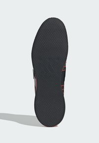 Sort sneakersål med et tekstureret gummimønster og en glat, buet form. Har røde accentlinjer på den laterale side.