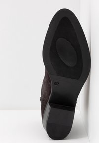 Zwarte suède enkellaars met een vierkante neus, gestructureerde rubberen zool en een verstevigde hiel, met een maatmarkering (37) aan de onderkant.