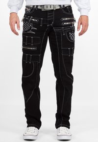 Pantaloni cargo neri con molte tasche con cerniera, cuciture bianche a contrasto e vestibilità slim. Presentano una cintura grigia e arrivano fino alla caviglia.