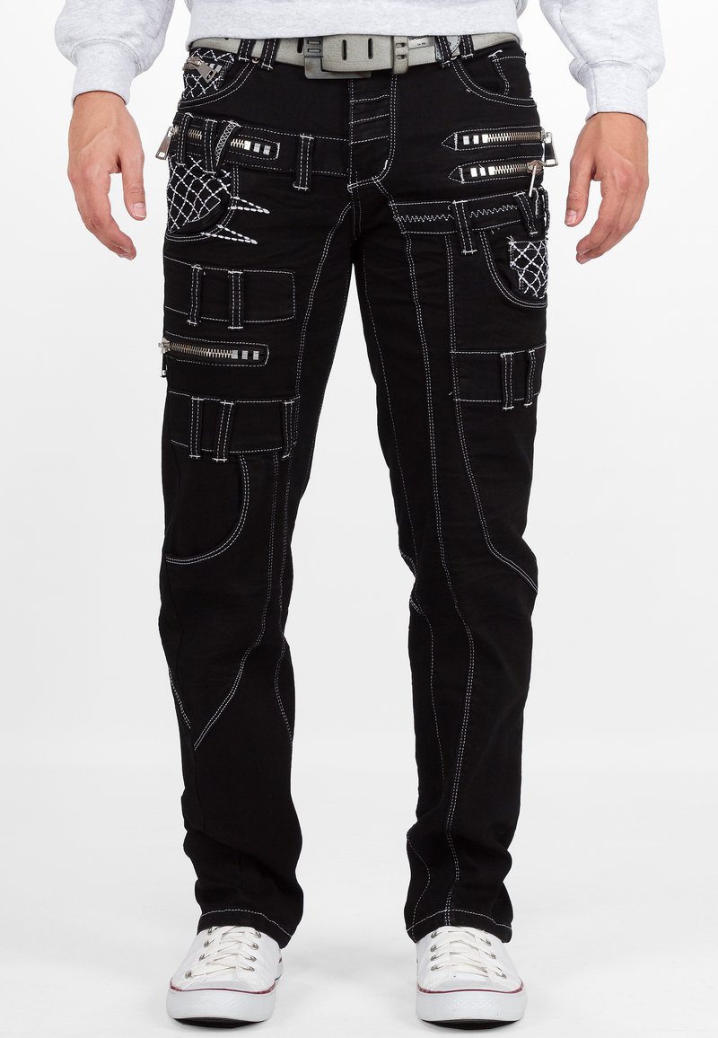 Pantaloni cargo neri con molte tasche con cerniera, cuciture bianche a contrasto e vestibilità slim. Presentano una cintura grigia e arrivano fino alla caviglia.