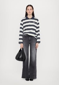 Marineblau- und weiße gestreifte Langarm-Polohemd mit Kragen, kombiniert mit hochgeschnittenen, ausgestellten dunkelgrauen Jeans und einer schwarzen Handtasche.