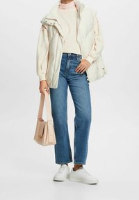 Chaleco acolchado blanco sobre un suéter rosa claro, combinado con jeans azules. Los accesorios incluyen un bolso rosa y zapatillas blancas.