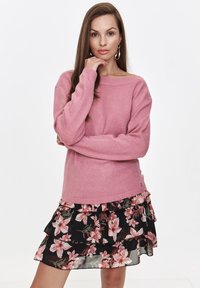 Różowy sweter dzianinowy o szerokim dekolcie i długich rękawach, w połączeniu z czarną, kwiecistą, warstwową spódnicą z różowymi kwiatami.