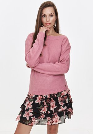 Różowy sweter dzianinowy o szerokim dekolcie i długich rękawach, w połączeniu z czarną, kwiecistą, warstwową spódnicą z różowymi kwiatami.