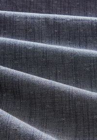 Mörkgrått tyg med en texturerad väv, som har subtila vertikala ränder och små prickmönster. Slät yta, lättviktig material.