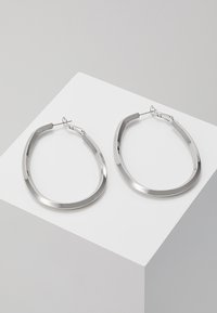 Sidabriniai auskarai žiedais, su glotnia ovalia forma ir lygiu paviršiumi. Turi hinged užsegimą, užtikrinantį saugų dėvėjimą.