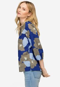 Blusa blu e grigia a fantasia con maniche a tre quarti, caratterizzata da una vestibilità morbida e un colletto rotondo, realizzata in tessuto leggero.