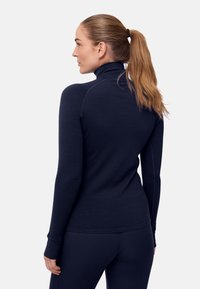 Mörkblå turtlenecktröja i texturerat tyg, med figurnära långa ärmar och formsydd siluett; bärs med matchande byxor.